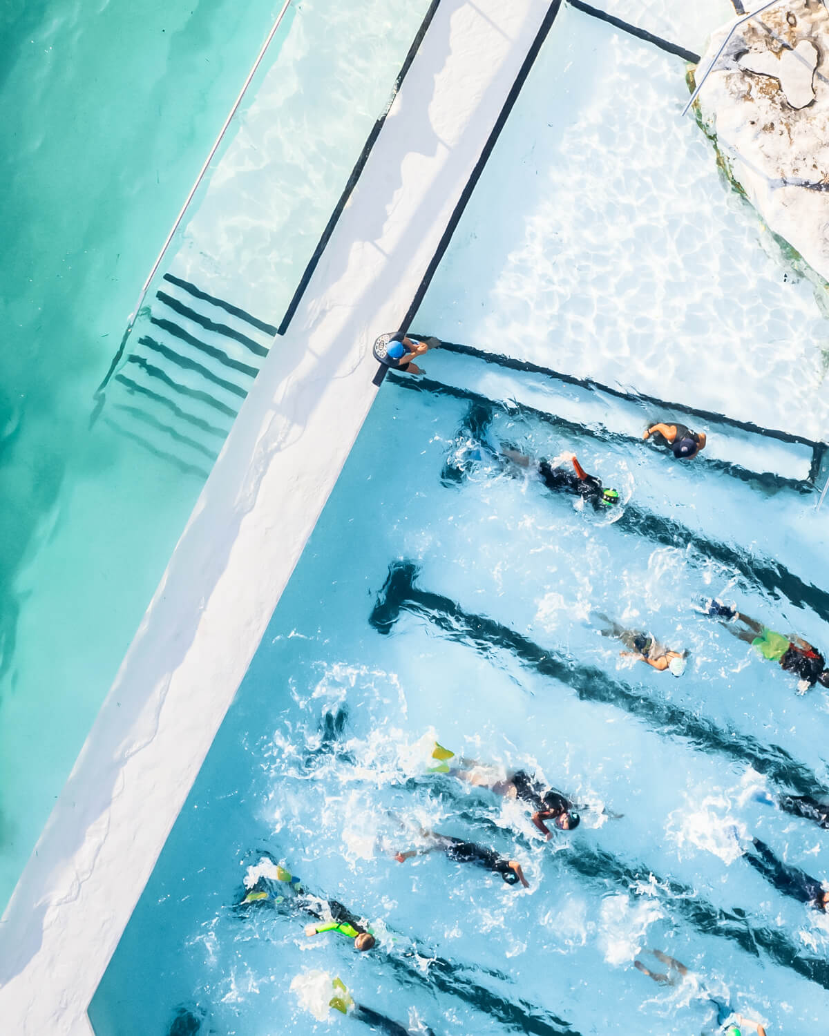 Aerial view of Bondi Icebergs pool with swimmers in lanes and ocean waves beyond the wall