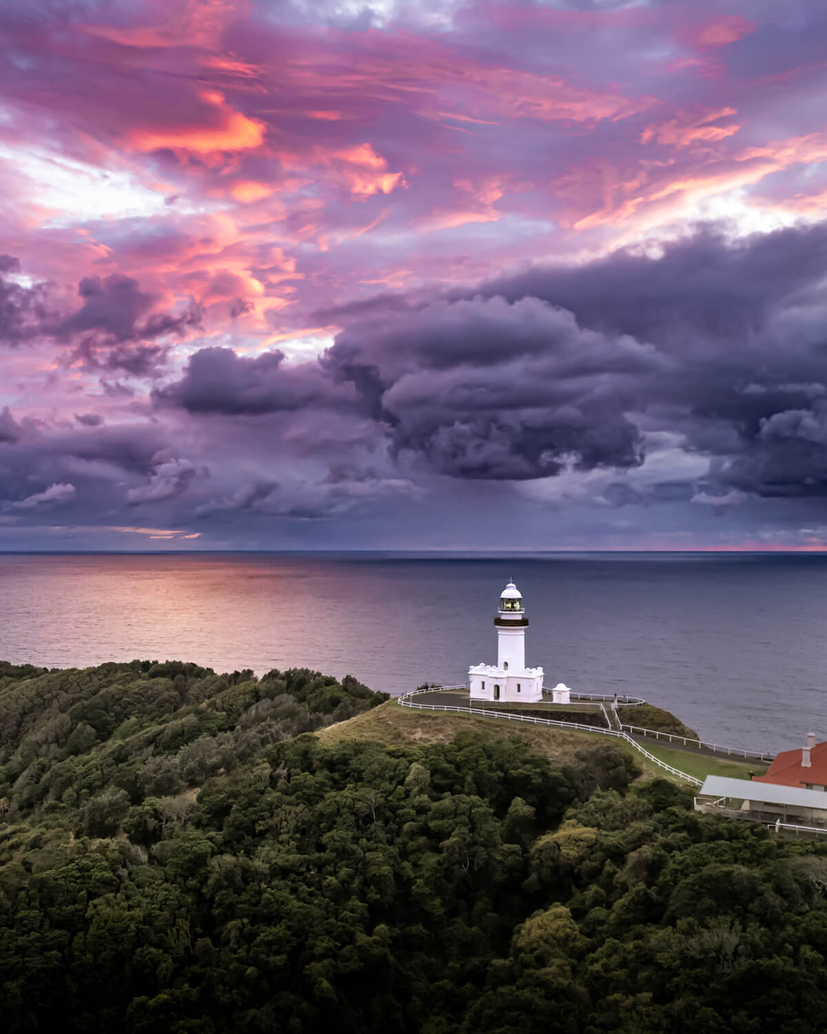 Aerial view of Cape Byron Lighthouse under dramatic purple and orange storm clouds at sunrise