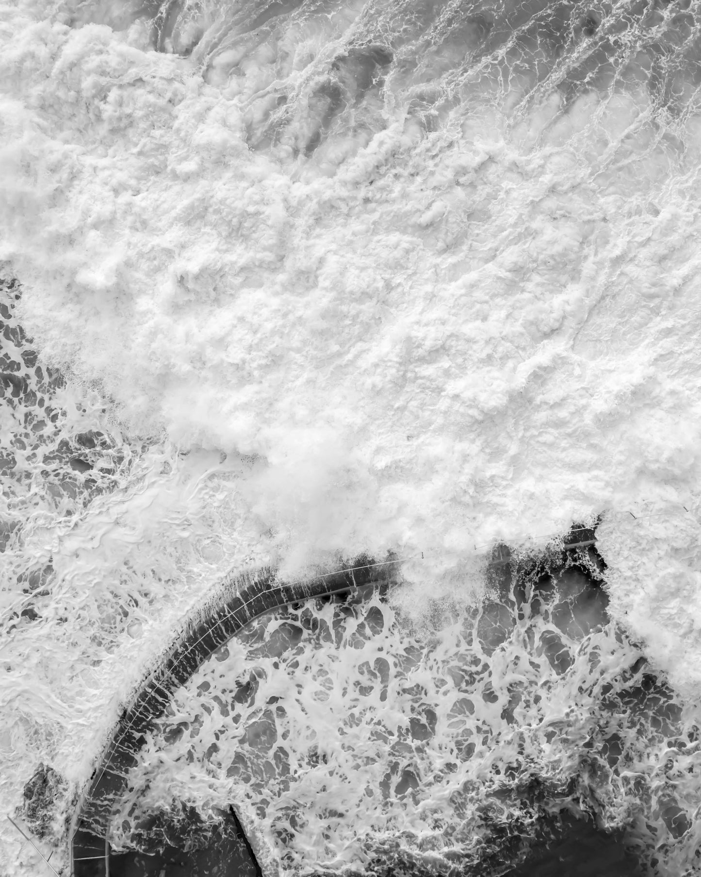 Aerial black and white photograph of Bronte rock pool engulfed by white water during a large swell, Sydney, by Nicolas Letoublon