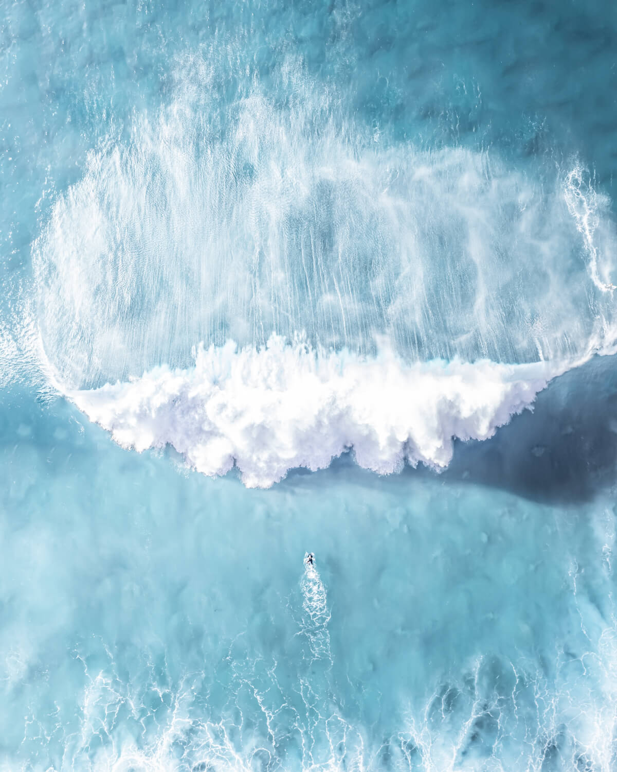 Aerial view of a lone surfer dwarfed by a massive wave at Bronte Beach, Sydney