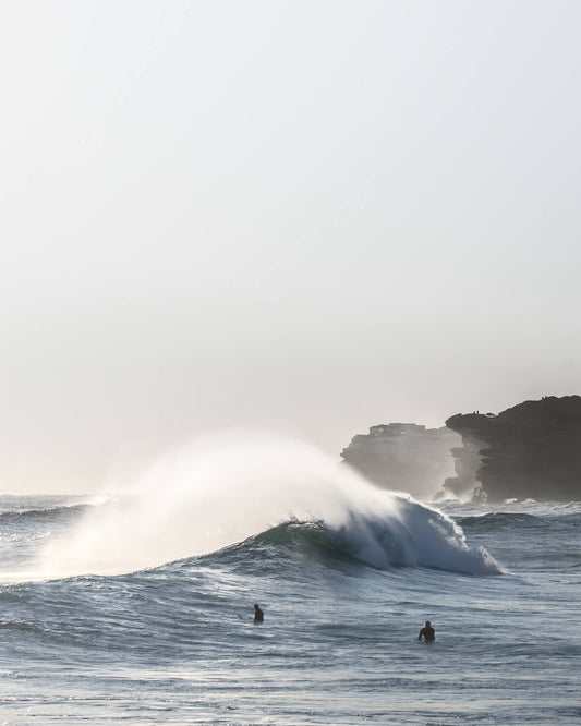 Ground-level view of a large winter wave breaking at Bronte Beach, Sydney, with two surfers watching from the water