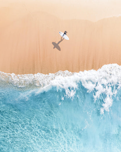 Aerial view of a lone surfer walking toward the breaking waves at Bronte Beach, Sydney