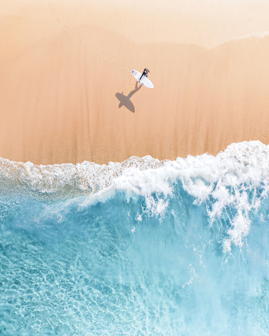 Aerial view of a lone surfer walking toward the breaking waves at Bronte Beach, Sydney