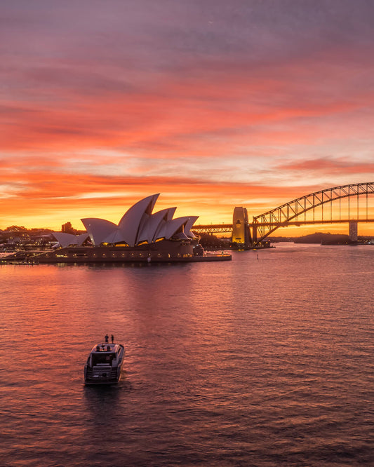 Aerial view of the Sydney Opera House and Harbour Bridge under a fiery orange sunset sky
