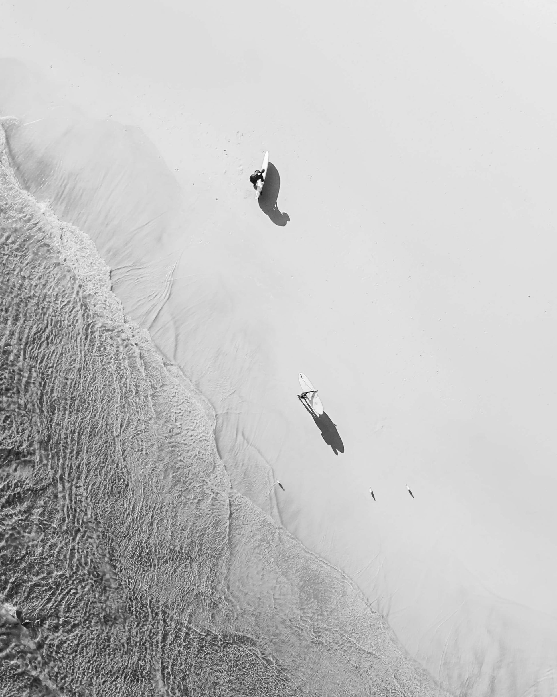 Aerial black and white photograph of two surfers walking on the beach at Byron Bay, Australia, by Nicolas Letoublon
